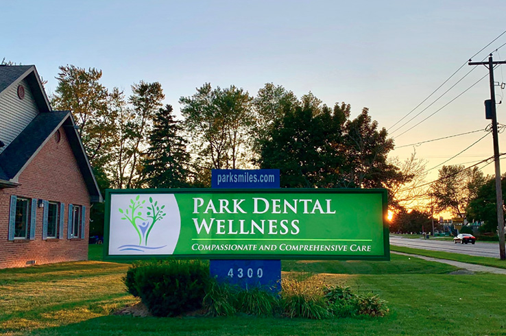 The image shows a sign for Park Dental Wellness with a tree logo, displayed at dusk outside a building with a green sign above it.