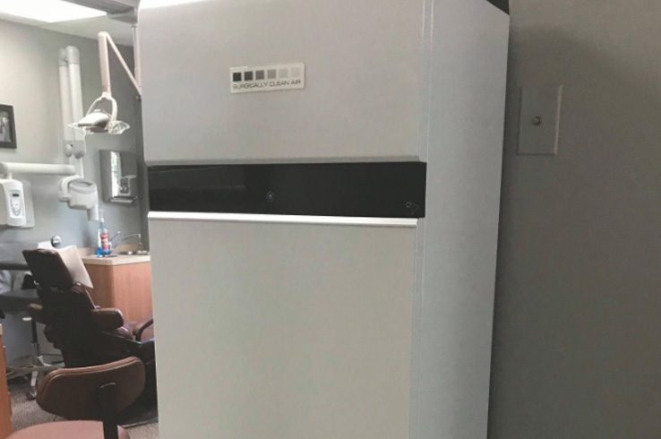 The image shows a large, metallic machine with a digital display inside a room, possibly a dental office, with a sign reading Dental X-Ray Machine on its side.