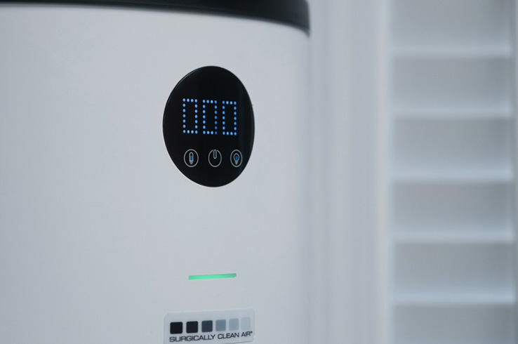 The image shows a modern digital thermostat with a display screen and buttons set against a refrigerator backdrop.