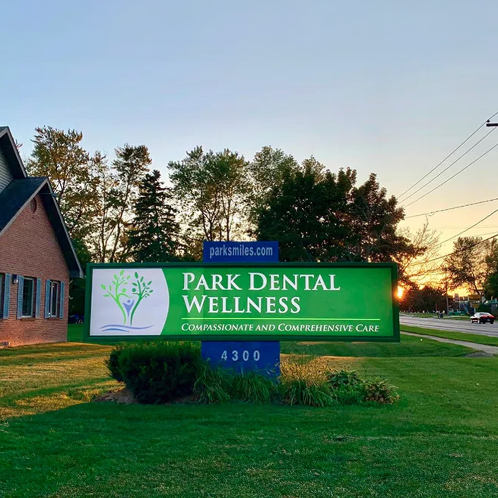 The image shows a sign for a dental practice named Park Dental Wellness with a website address provided, set against a backdrop of a building at dusk.