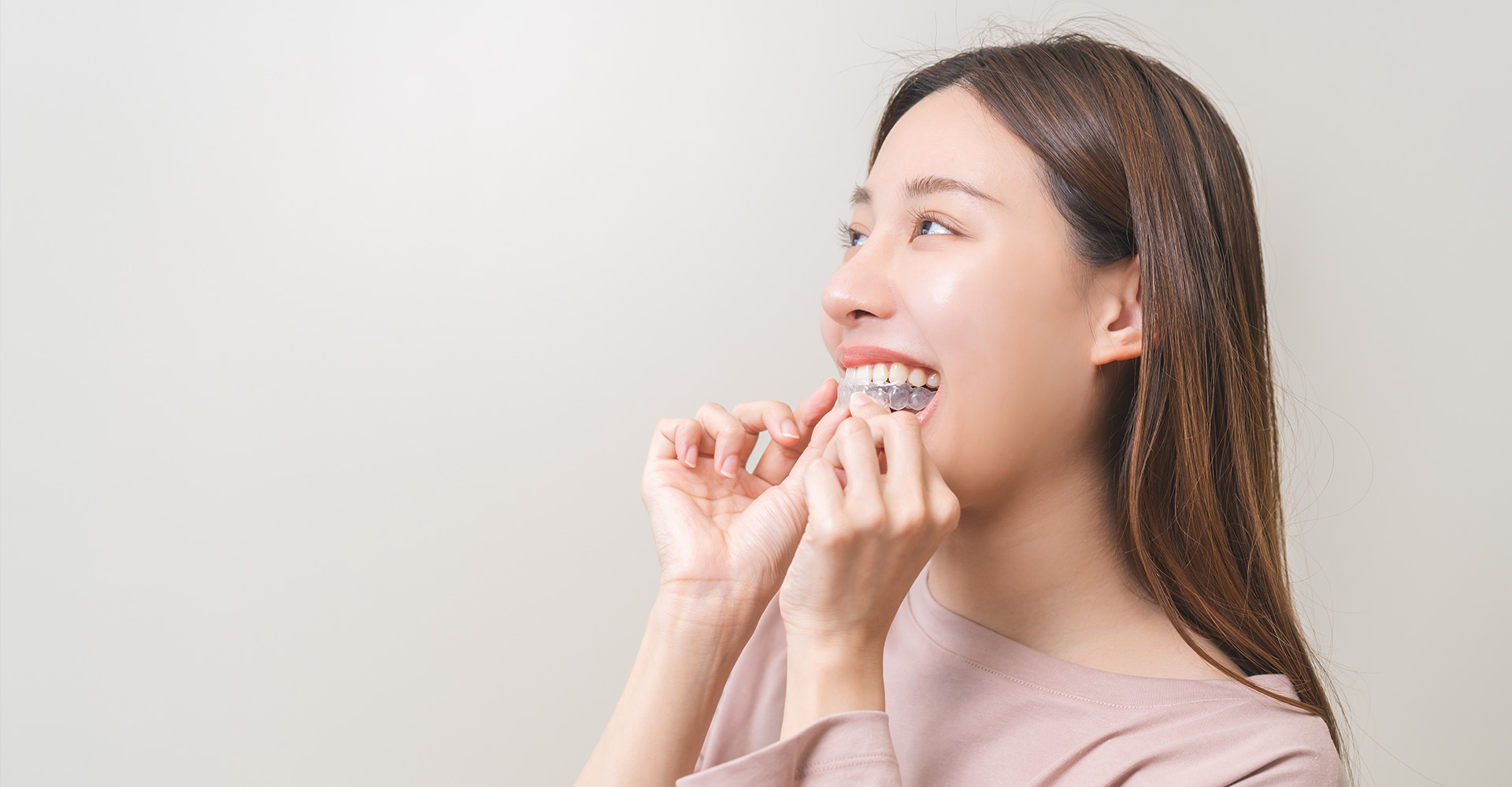 A woman with a toothbrush in her mouth, smiling at the camera, against a white background.