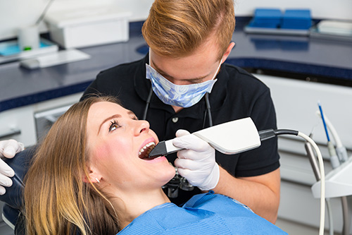 The image shows a dental hygienist performing a teeth cleaning procedure on a patient who is seated in a dentist s chair, with various dental equipment and tools visible around them.