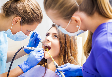 The image shows three individuals engaged in dental care procedures, with one person receiving treatment while two others assist using dental instruments and a mask.