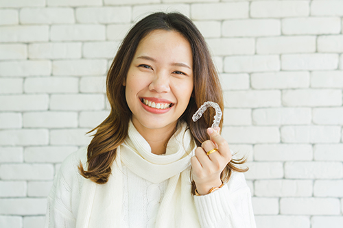 A woman with a bright smile holding a toothbrush up to her mouth against a brick wall background.