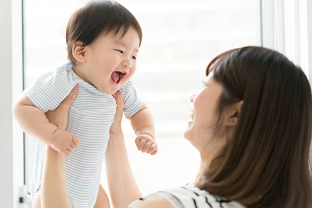 A woman holding a baby while smiling, with both of them indoors.